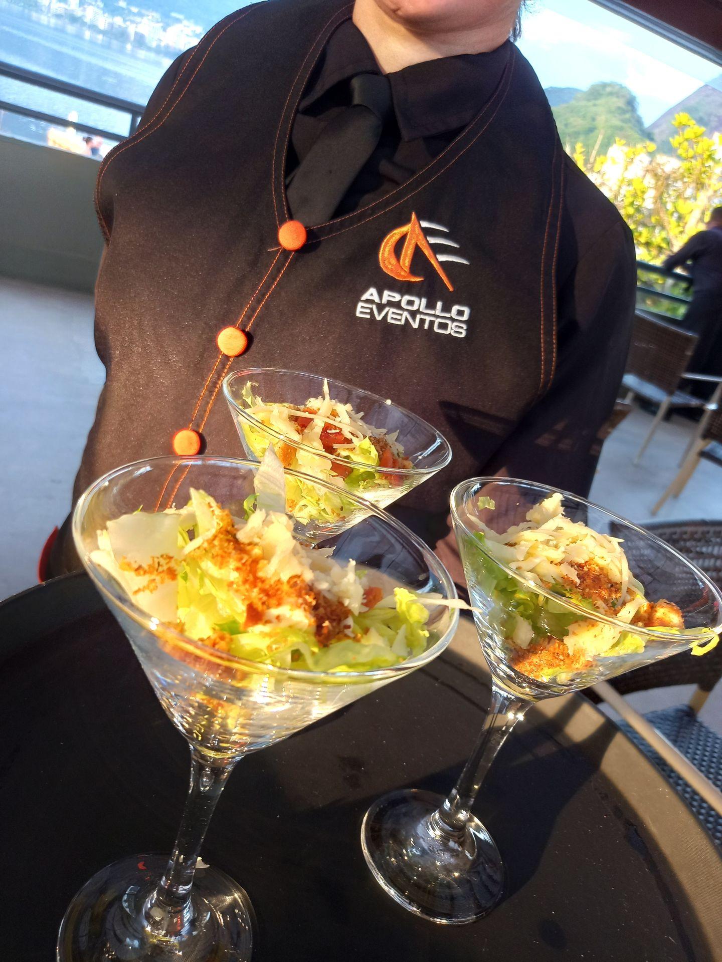 Server holding a tray with Caesar salad in martini glasses at an outdoor event.